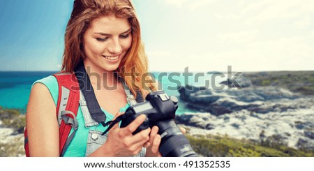adventure, travel, tourism, hike and people concept - happy young woman with backpack and camera photographing over seashore or beach background
