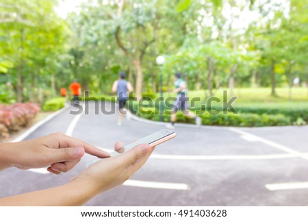 Man use mobile phone, blur image of people exercise in the park as background.