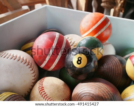 An old eight ball in wooden bin full of vintage game balls, including pool, croquet, and baseball.
