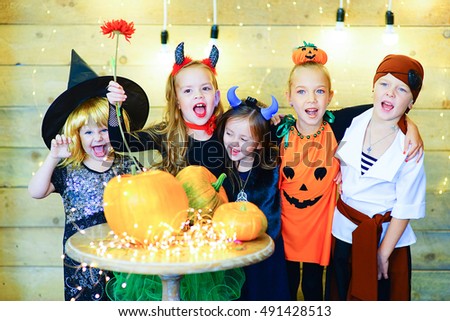 Happy group of witch children, pirate and demons during Halloween party playing around the table with pumpkins