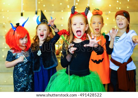 Happy group of witch children, pirate and demons during Halloween party playing around the table with pumpkins