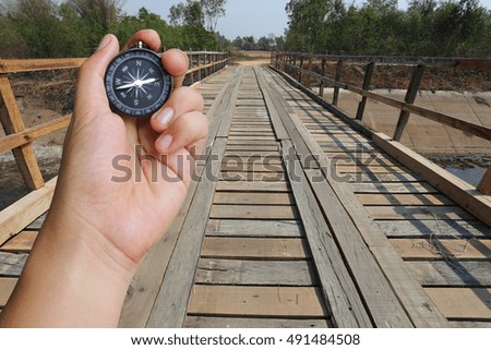 hand of a man holding a compass and wood bridge in the countryside,concept of journey or traveling.