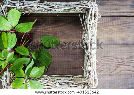 Empty picture frame decorated wild grapes. Wicker frame on the cover of old wooden background.