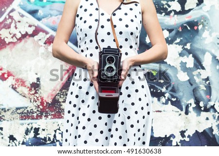 Horizontal view of a woman in dotted dress holding a camera against a graffiti wall