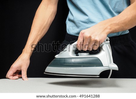 Male person using a steaming hot iron, on a iron board on black