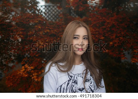 Happy Asian Girl in a park during Autumn season. Portrait of a young Asian woman with autumn trees on the background. Woman portrait in a park in Autumn Season

