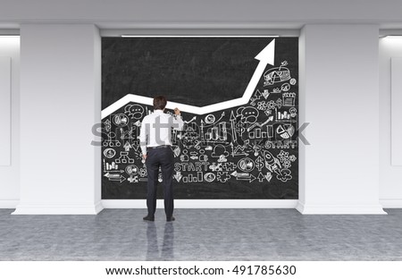 Rear view of man drawing white growing graph and business sketches at blackboard in office lobby. Concept of company growth. 3d rendering. Mock up