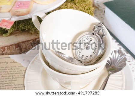 Close up porcelain teacup with pocket watch. Blur invitation card. Afternoon Tea party. Alice in Wonderland's Mad Tea Party concept.