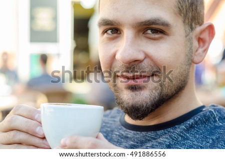 Beautiful natural man looking at the camera and drinking coffee, eyes laughing
