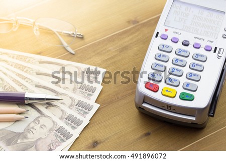 Credit Card Terminal or EDC on cashier wooden table in the store with japanese bank notes, pen, pencil and calculator.