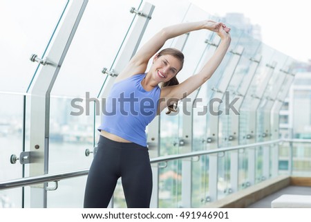 Smiling sporty woman stretching body on balcony