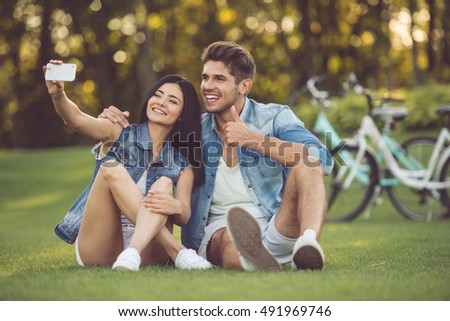 Beautiful stylish couple is doing selfie using a smart phone and smiling while resting in the park