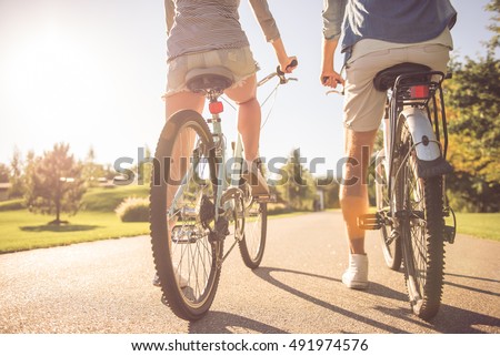 Back view of beautiful stylish couple cycling in the park, cropped