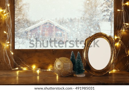 Old window sill with gold christmas lights and empty vintage frame in front of dreamy and magical winter snow landscape background. Ready to put photography