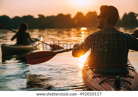Meeting sunset on kayaks. Rear view of young couple kayaking on lake together with sunset in the backgrounds Royalty-Free Stock Photo #492010117
