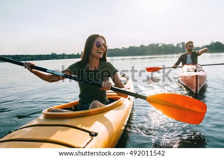 Couple kayaking together. Beautiful young couple kayaking on lake together and smiling  Royalty-Free Stock Photo #492011542