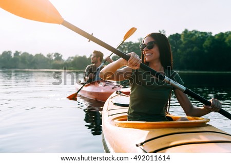 Nice day for kayaking. Beautiful young couple kayaking on lake together and smiling 
