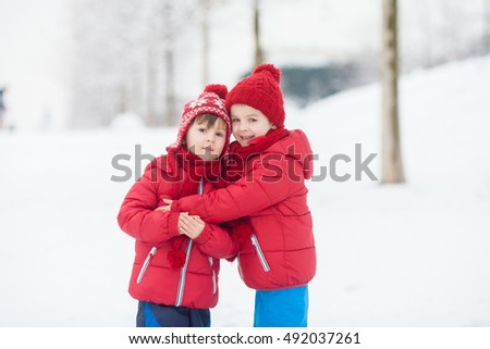 Two adorable children, boy brothers, playing in a snowy park, holding hands and hugging