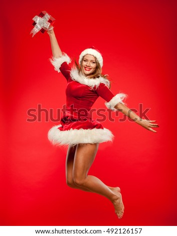 christmas, x-mas, winter, concept - smiling woman in santa helper hat with gift box, happiness jump for joy over red background