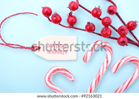 Festive Christmas background close up with decorated borders of red and white candy canes, berries and Happy Holidays gift tag on a pale blue wood table. 