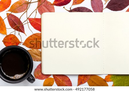 Open notepad with autumn falling leaves and cup of coffee. Top view