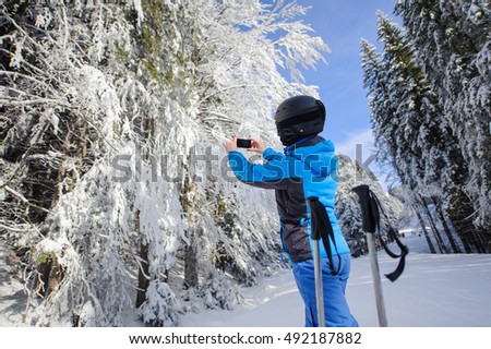 Rear view of woman taking picture with her cell phone in the winter forest with beautiful trees on ski slope. Winter sports concept. Carpathian Mountains, Bukovel, Ukraine