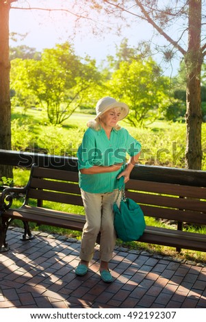 Elderly woman holding her stomach. Lady near park bench. Strong pain under ribs. Signs of chronic illness.