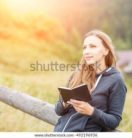 Young hiker woman sketching into notebook resting near fence in mountains