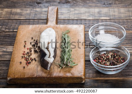 Fresh halibut fish steak on a vintage board with salt, pepper and rosemary. Over wooden background. 