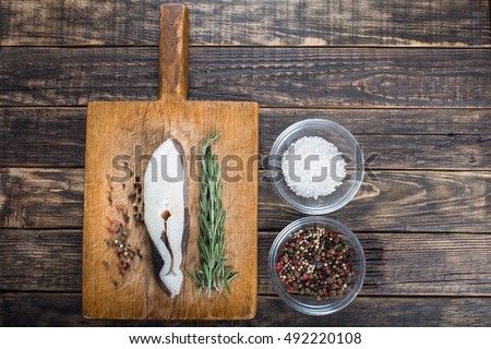 Fresh halibut fish steak on a vintage board with salt, pepper and rosemary. Over wooden background. Top view