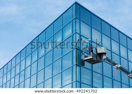 Washer washing the windows of modern skyscraper Royalty-Free Stock Photo #492241702