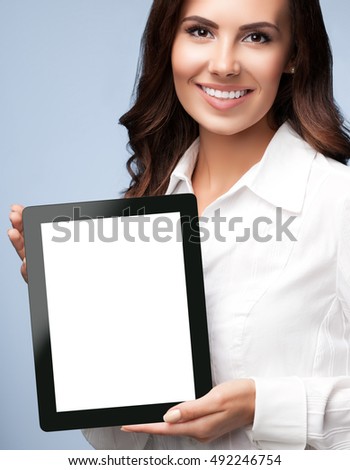 Smiling young businesswoman showing blank no-name tablet pc monitor, over grey background, with copyspace area for slogan or text message. Caucasian brunette model in business concept shoot.