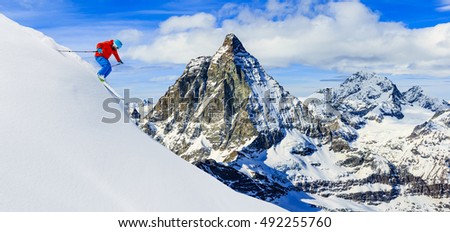 Skier skiing downhill in high mountains in fresh powder snow. Snow mountain range with Matterhorn in background. Zermatt Alps region Switzerland. Royalty-Free Stock Photo #492255760