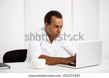 Young successful african businessman typing on laptop, sitting at workplace.