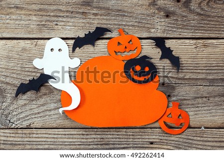 Cloud frame with ghost, pumpkin and bats cut out of paper. Happy Halloween card. Background of old wooden boards.