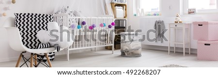 Spacious, light child room with white cot, chairs and colorful decorations, panorama