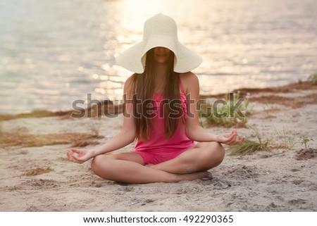 Young teen girl doing yoga meditation on nature.Good looking slim teenage female model meditate on seaside at sunset.Young white girl meditating outdoor in sunny evening.Healthy lifestyle background