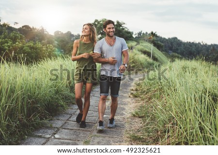 Outdoor shot of young couple in love walking on pathway through grass field. Man and woman walking along tall grass field. Royalty-Free Stock Photo #492325621