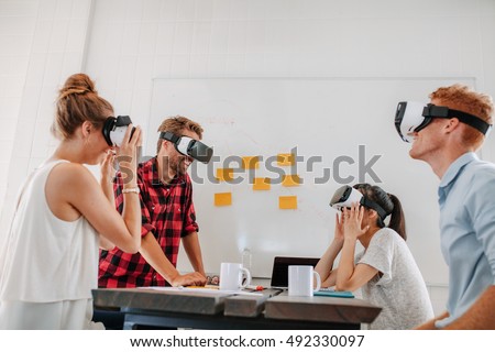 Business team using virtual reality headset in office meeting. Developers meeting with virtual reality simulator around table in creative office.