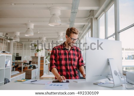 Shot of happy young man working on desktop computer in modern workplace. Young entrepreneur working at start up. Royalty-Free Stock Photo #492330109
