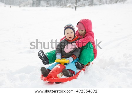 Brother and sister playing in the snowy winter landscape, hugging, sledding, having winter fun. Active family lifestyle,  bonding, natural childhood, fun and carefree childhood concept.  
