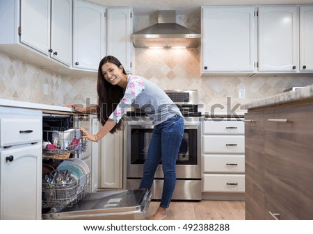 happy young woman putting dishes into the dishwasher in her modern kitchen