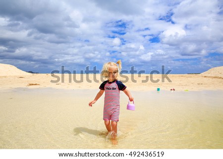 Beautiful blond-haired girl walking in the water on sandy beach with blue sky background and white clouds. Oahu , New Zealand
