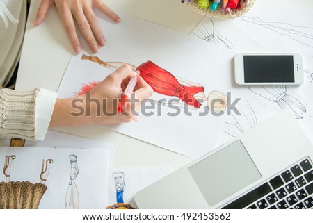 Hands colouring a clothing design sketch in red. Concept photo, top view, closeup, close-up