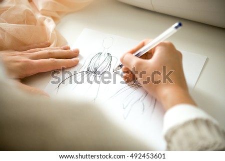 Hands drawing a black ink clothing design sketch, view over the shoulder, closeup, close-up