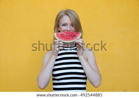 Beautiful young woman holding slice of watermelon and smiling on yellow wall background