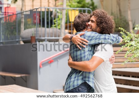 Cheerful best friends embracing each other outside coffee shop. Two young multiethnic guys hugging each other. Happy smiling best friends meeting each other after a long time with a hug. Royalty-Free Stock Photo #492562768