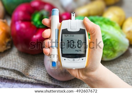 Diabetic diet and diabetes concept. Hand holds glucometer. Vegetables in background. Royalty-Free Stock Photo #492607672