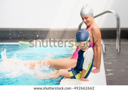 Little boy and instructor splashing on swimming class on the edge of pool