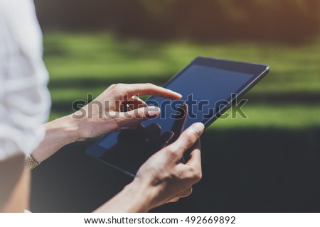 Hipster young girl using tablet or holding gadget, planning travel plan. Female hands holding computer, tourist traveler texting message on device on green background. Mockup for text, flare and bokeh
